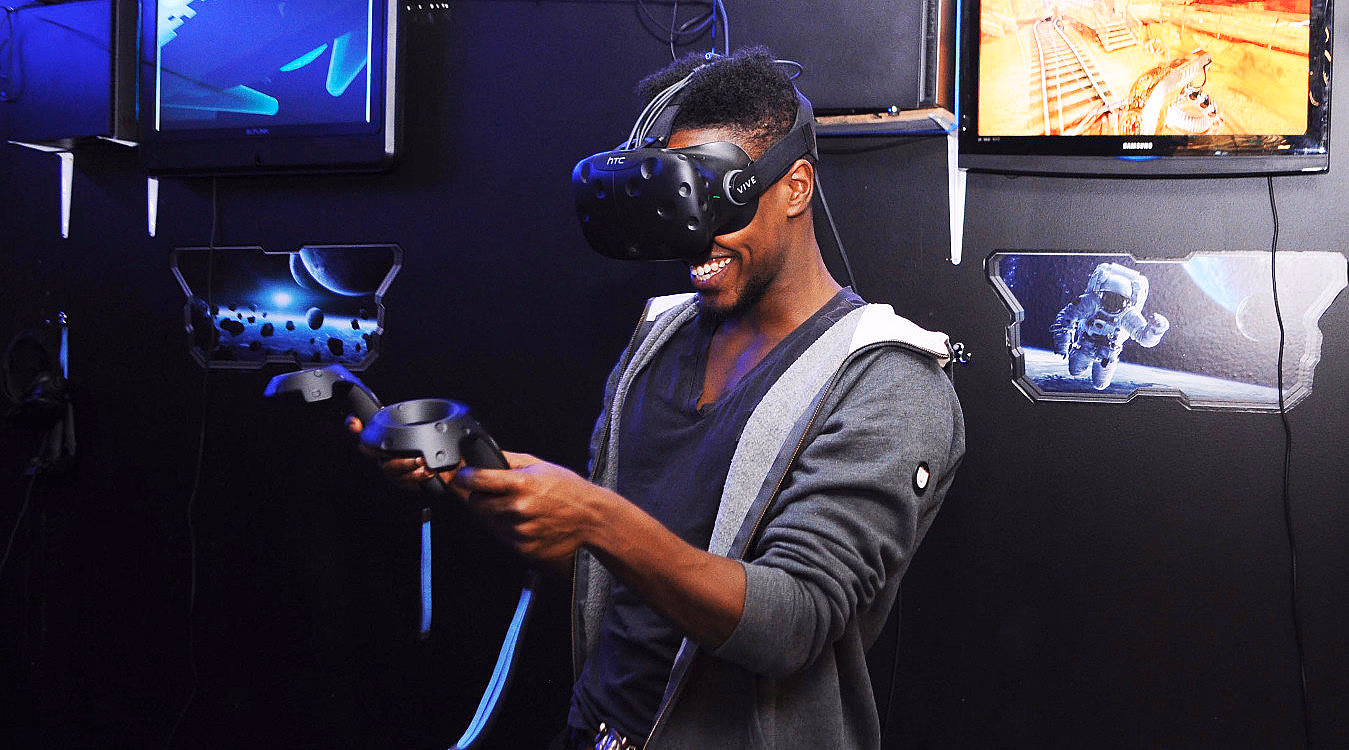Person med VR-briller og kontrollere i et rom med blå belysning og romfartsmotiver