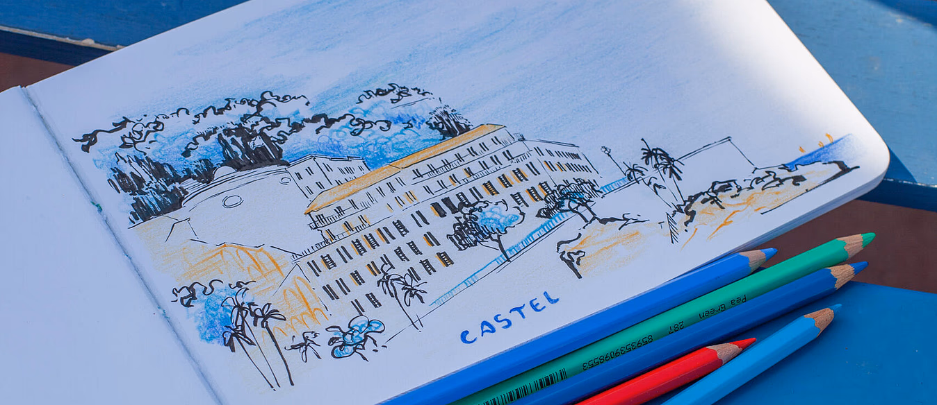 Åpen skissebok på en blå benk med tegning merket CASTEL og fem fargeblyanter