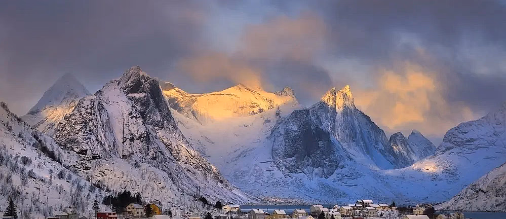 Snødekte fjell og rorbuer ved vannet i Lofoten om vinteren