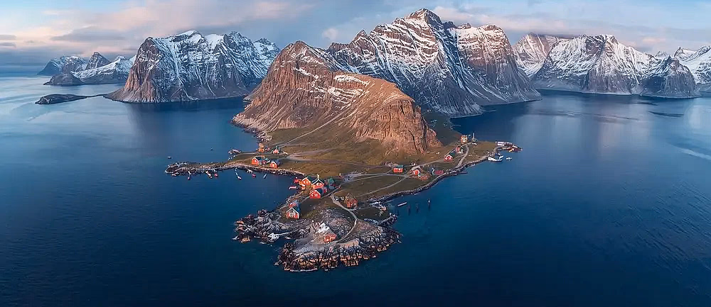 To personer i en rød kajakk på vannet med fjell i bakgrunnen