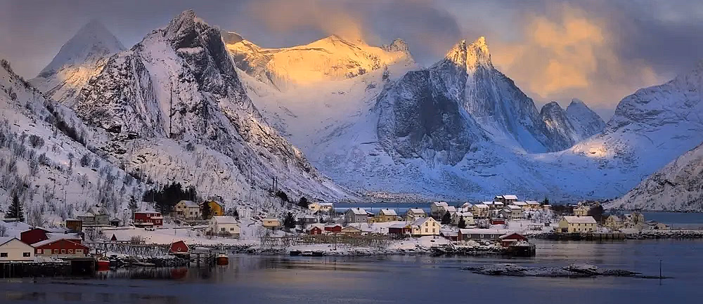 Snødekte fjell og rorbuer ved vannet i Lofoten om vinteren