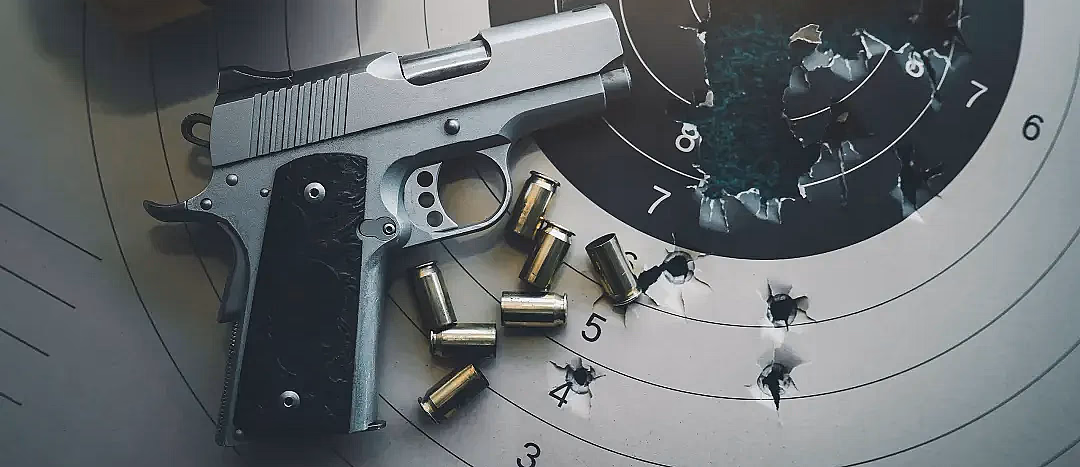 Sølvfarget pistol med svart grep på en papirblink med kulehull, tomhylser i messing og gule hørselvern.