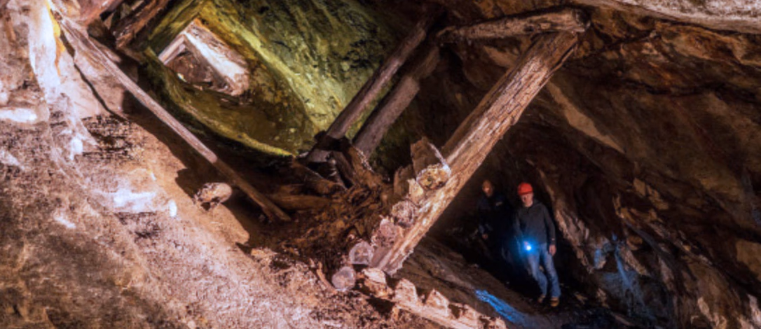 To personer med hjelmer og lommelykt i en trang, steinete tunnel med trebjelker