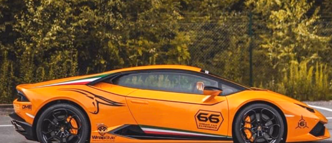 Oransje sportsbil med tallet 66 og fargede striper parkert på grå asfalt