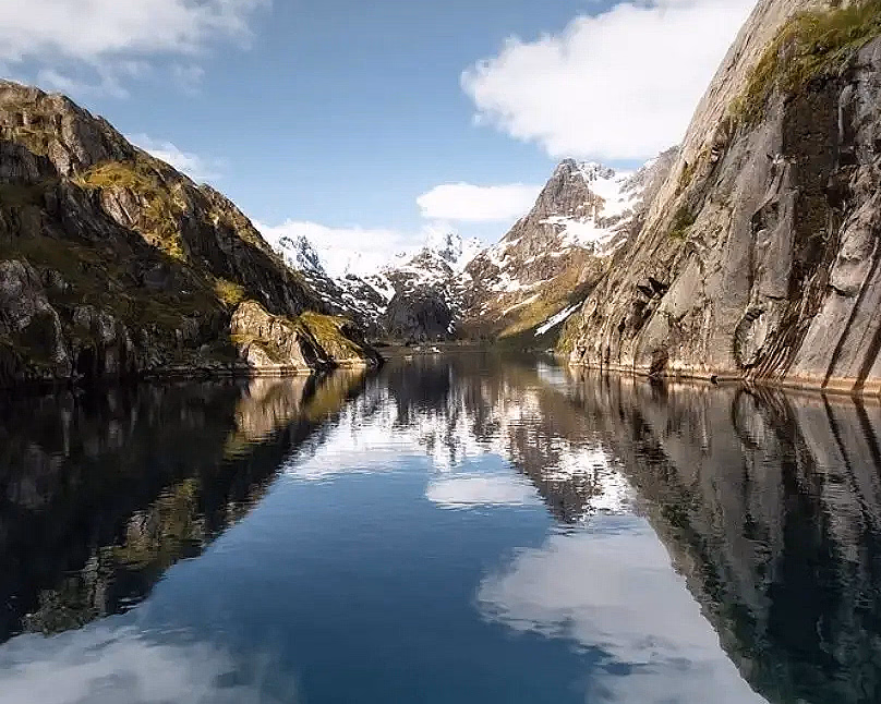 Passasjerbåt i en smal fjord med bratte fjellsider og snø på toppene