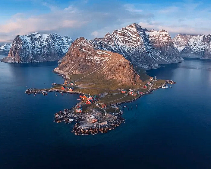 To personer i en rød gummibåt på vannet foran høye, snødekte fjell i Lofoten