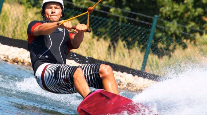 Person på wakeboard med hvit hjelm og rødt brett på vannet