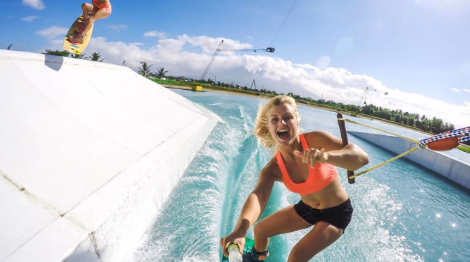 Person i rosa topp og svarte shorts på wakeboard på vannet ved en rampe