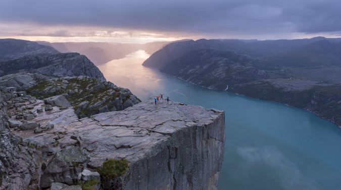 Mennesker på en flat fjellhylle over en fjord med fjell i bakgrunnen