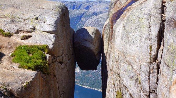 Stor rund stein kilt fast mellom to fjellvegger over en dyp fjord