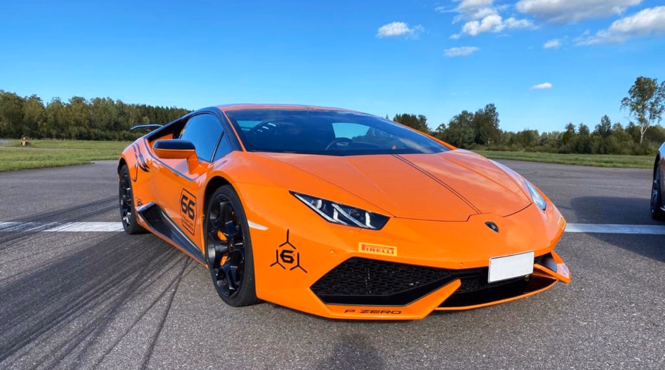 Oransje sportsbil med Pirelli-dekal og nummer 66 parkert på en asfaltert bane