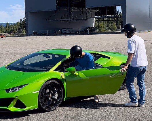 En limegrønn sportsbil med svarte felger på en asfaltert plass. Førerdøren er åpen, og to personer med hjelmer står ved bilen foran en stor grå hangar med skiltet "MSG PRODUCTION AS".