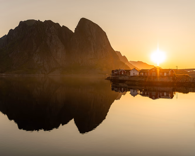 To personer som sitter på en fjelltopp og ser utover havet og fjellene i midnattssol