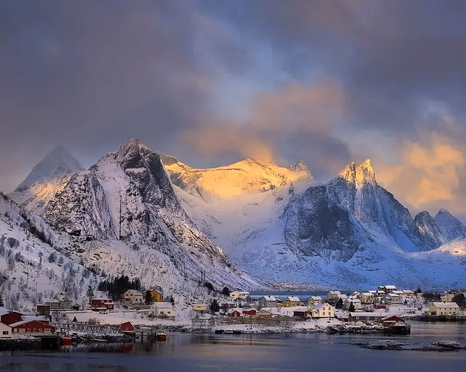 Snødekte fjell og rorbuer ved vannet i Lofoten i vintersol