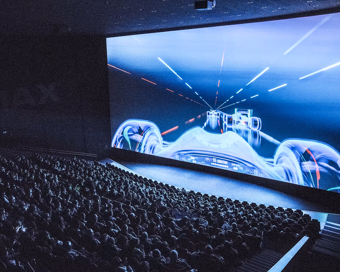 Publikum i en kinosal som ser på en stor skjerm med racerbilmotiv og IMAX-logo på veggen
