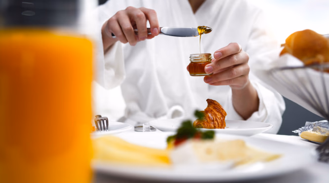 Person i hvit morgenkåpe med honning, croissant, ost og appelsinjuice på et frokostbord