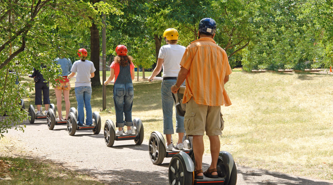 Fem personer med fargerike hjelmer kjører Segway på en asfaltert sti i en park