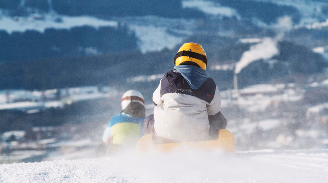 To personer aker ned en snøbakke med snøsprut rundt seg
